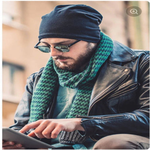 Man wearing a blue beanie, green scarf, and sunglasses using a tablet.